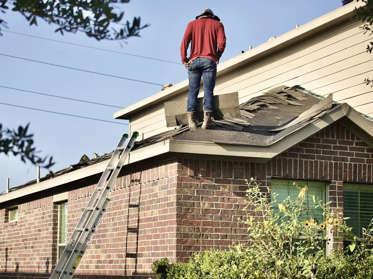 Roof Replacement in La Porte — a roofer standing on the roof of a brick house with a ladder against the eave