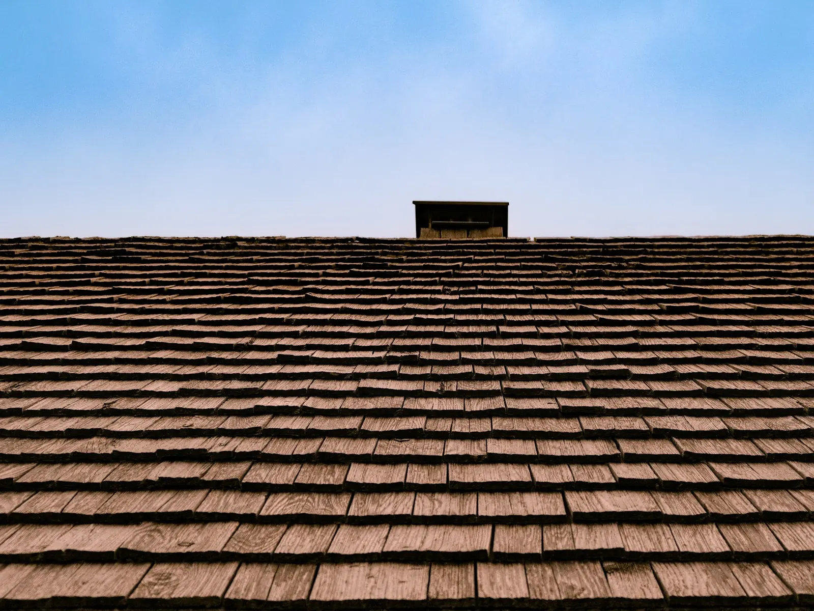 Roof Replacement in La Porte — a brown asphalt shingle roof and chimney against a blue sky